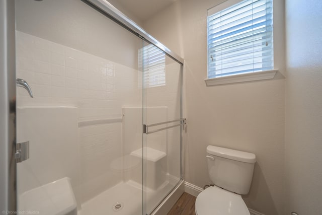 bathroom featuring hardwood / wood-style flooring, plenty of natural light, toilet, and a shower with shower door