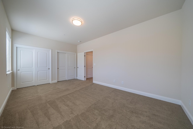 unfurnished bedroom featuring light colored carpet and multiple closets