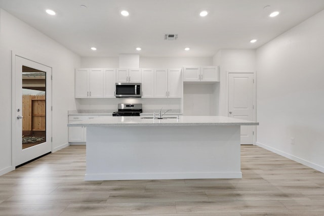 kitchen with sink, light hardwood / wood-style flooring, an island with sink, white cabinetry, and stainless steel appliances