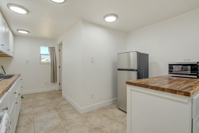 kitchen with white cabinetry, sink, wooden counters, light tile patterned floors, and appliances with stainless steel finishes