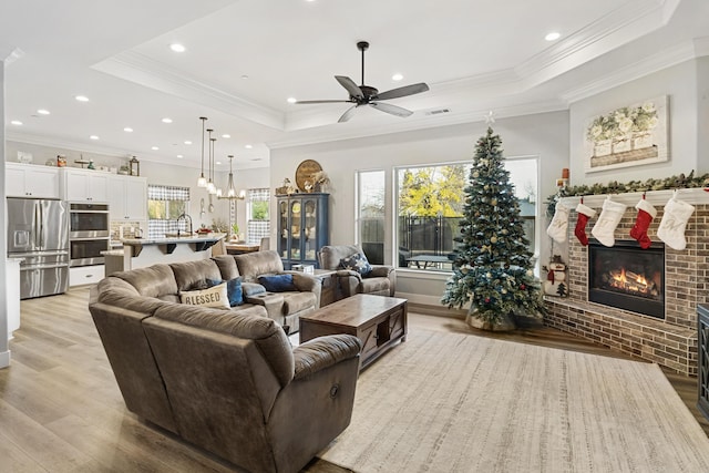 living room with ornamental molding, a tray ceiling, ceiling fan, light hardwood / wood-style flooring, and a fireplace