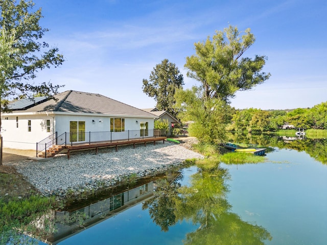 back of property with a water view and solar panels