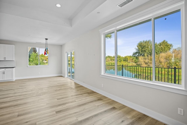 interior space featuring a raised ceiling, a water view, and light hardwood / wood-style floors