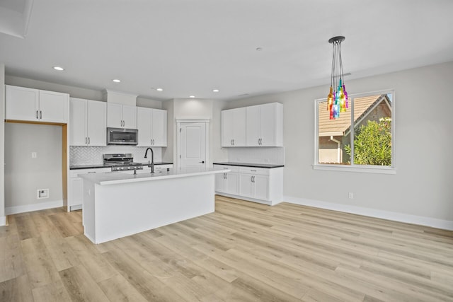 kitchen featuring a kitchen island with sink, white cabinets, hanging light fixtures, appliances with stainless steel finishes, and light hardwood / wood-style floors