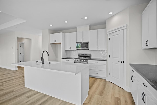 kitchen with white cabinetry, sink, a center island with sink, appliances with stainless steel finishes, and light wood-type flooring