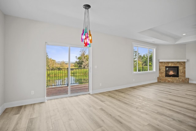 unfurnished living room featuring a water view, light hardwood / wood-style floors, a tray ceiling, and a premium fireplace