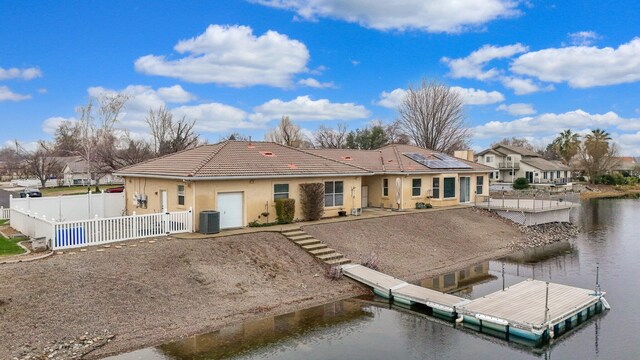 rear view of house with solar panels, cooling unit, and a water view