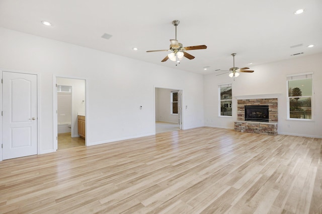 unfurnished living room featuring light wood-type flooring, a stone fireplace, and ceiling fan