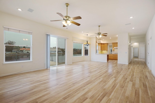 unfurnished living room featuring ceiling fan with notable chandelier and light hardwood / wood-style flooring