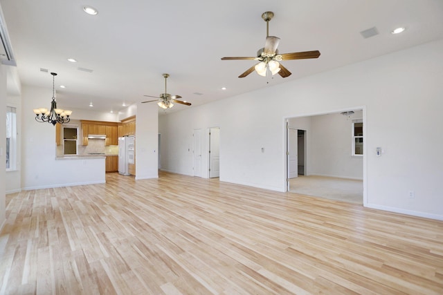 unfurnished living room featuring ceiling fan with notable chandelier and light wood-type flooring