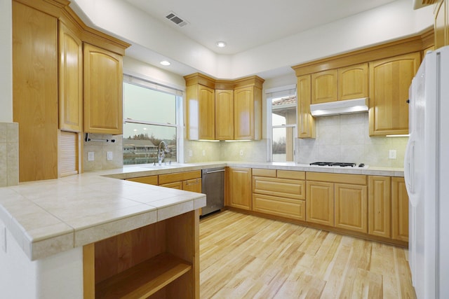 kitchen with backsplash, kitchen peninsula, tile countertops, white fridge, and light hardwood / wood-style floors