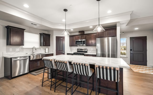 kitchen featuring a center island, sink, stainless steel appliances, pendant lighting, and a tray ceiling