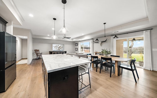 kitchen featuring stainless steel refrigerator, light stone countertops, a center island, decorative light fixtures, and a tray ceiling