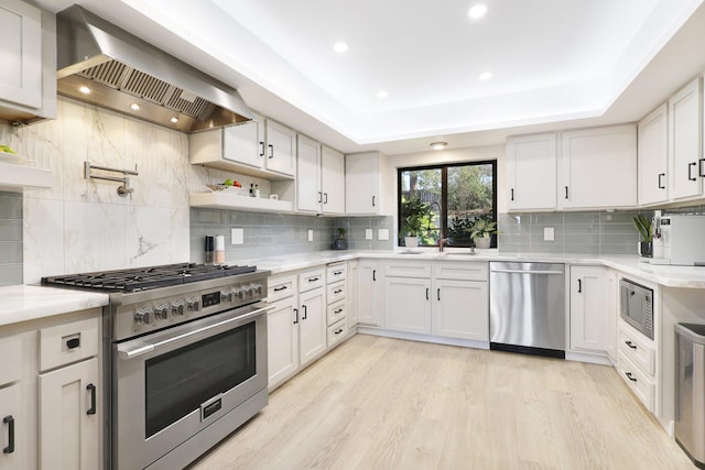 kitchen featuring light wood-type flooring, stainless steel appliances, white cabinetry, and wall chimney range hood