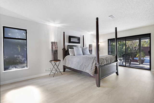 bedroom with access to exterior, light hardwood / wood-style floors, and a textured ceiling