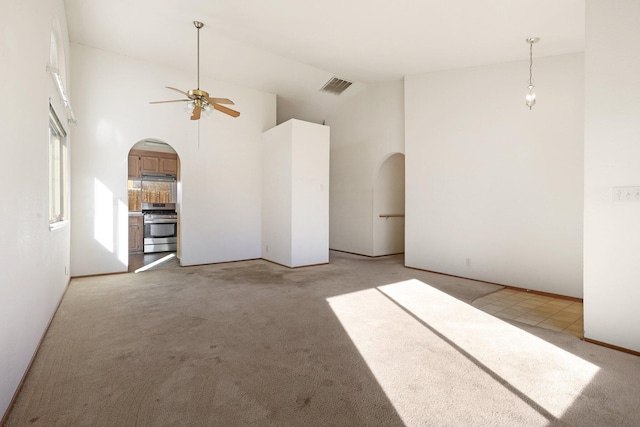 unfurnished living room featuring a towering ceiling, light colored carpet, and ceiling fan