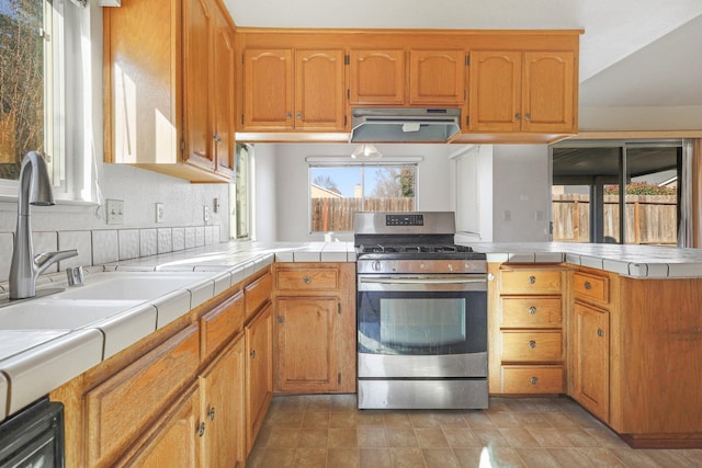 kitchen featuring sink, backsplash, stainless steel range with gas stovetop, extractor fan, and tile countertops