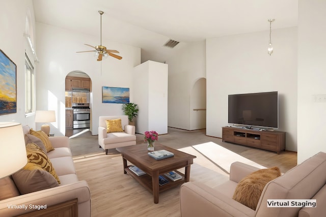 living room featuring ceiling fan, a towering ceiling, and light wood-type flooring