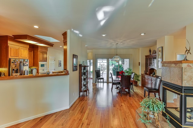 kitchen featuring stainless steel refrigerator with ice dispenser, a skylight, white microwave, decorative light fixtures, and light hardwood / wood-style floors