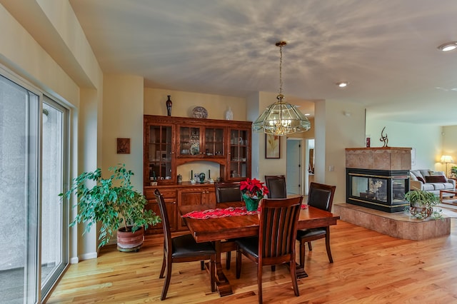 dining space with a tile fireplace, a notable chandelier, and light wood-type flooring