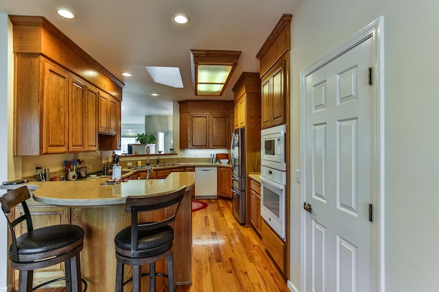 kitchen featuring a breakfast bar, white appliances, light hardwood / wood-style flooring, a skylight, and kitchen peninsula