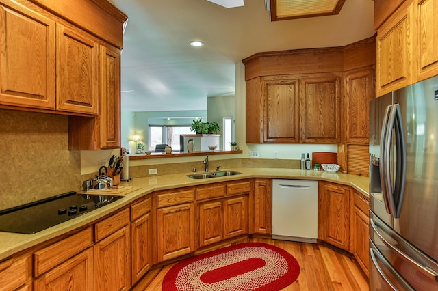 kitchen with dishwasher, black electric stovetop, sink, stainless steel fridge, and light wood-type flooring