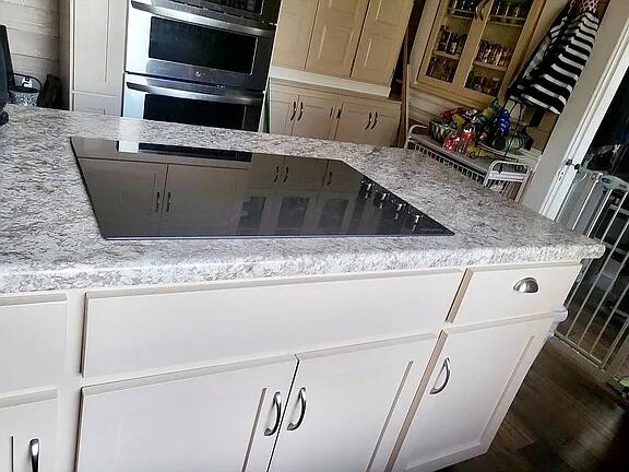 kitchen featuring white cabinets, light stone countertops, and double oven