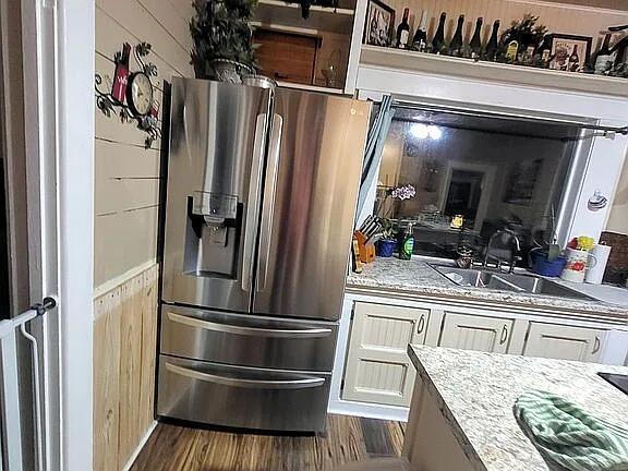 kitchen featuring white cabinets, stainless steel fridge, light stone counters, and sink