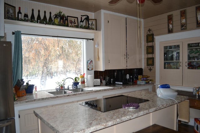 kitchen with sink, backsplash, stainless steel fridge, black electric cooktop, and white cabinets