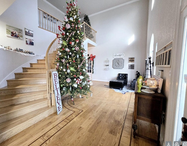 stairway with wood-type flooring, ornamental molding, and a towering ceiling