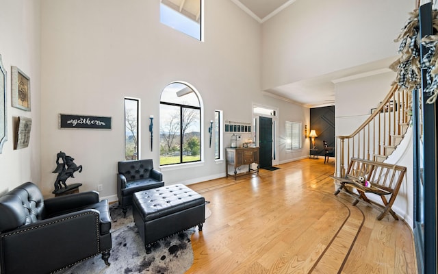 sitting room with a towering ceiling, ornamental molding, and light hardwood / wood-style flooring