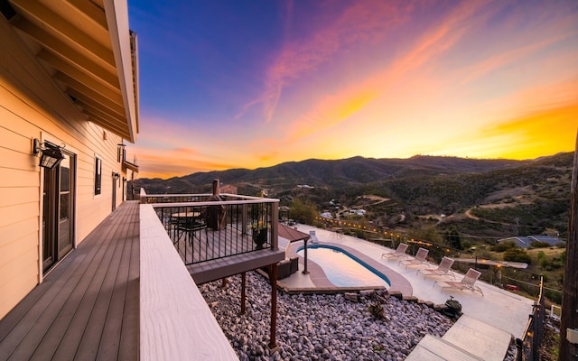 deck at dusk featuring a fenced in pool and a mountain view