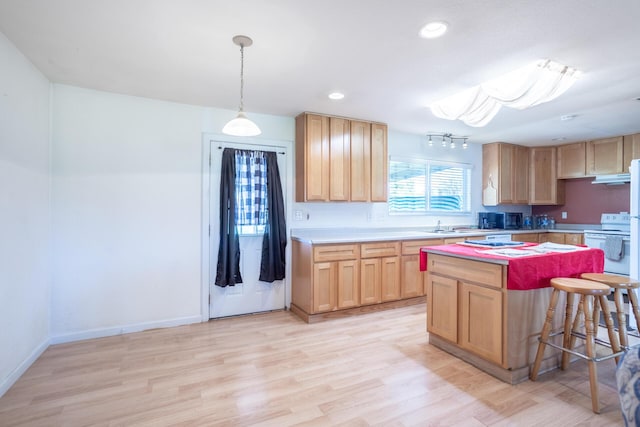 kitchen featuring light wood finished floors, light brown cabinetry, light countertops, under cabinet range hood, and a center island