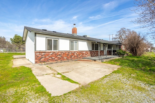 rear view of house featuring a chimney, a patio area, brick siding, and a lawn