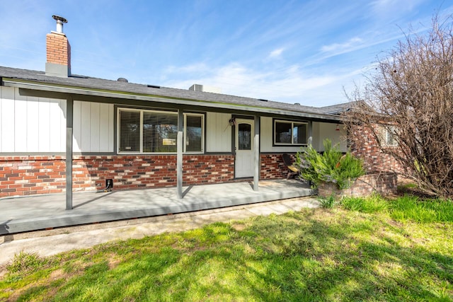 back of property with brick siding, board and batten siding, a chimney, and a yard