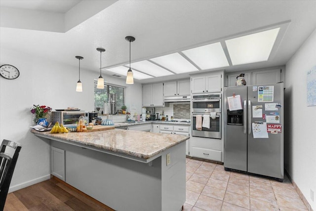 711 Teakwood Dr, Redding, CA 96003 - kitchen with appliances with stainless steel finishes, a peninsula, under cabinet range hood, decorative light fixtures, and a sink
