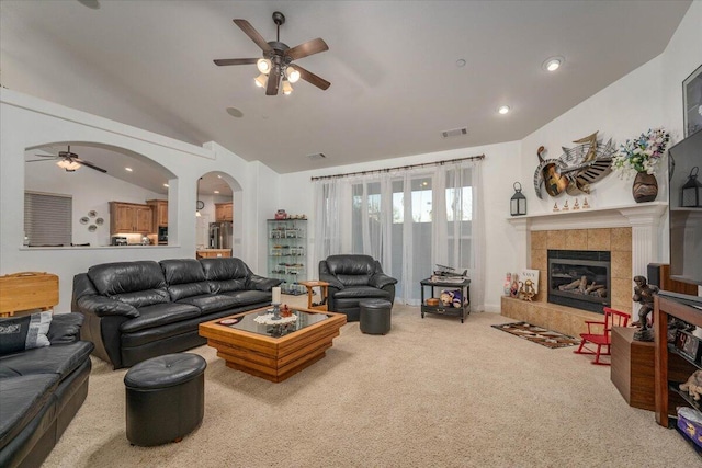 living room featuring a tile fireplace, light carpet, ceiling fan, and vaulted ceiling