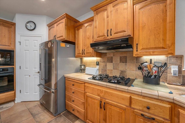 kitchen with light tile patterned floors, backsplash, tile counters, and black appliances