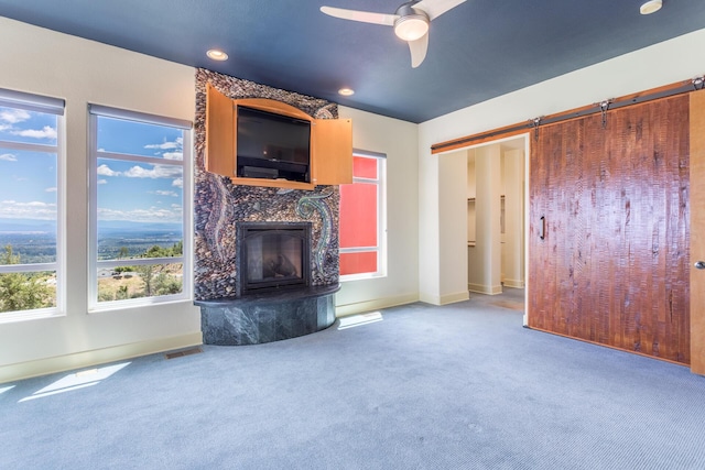 unfurnished living room with a high end fireplace, carpet floors, ceiling fan, and a barn door