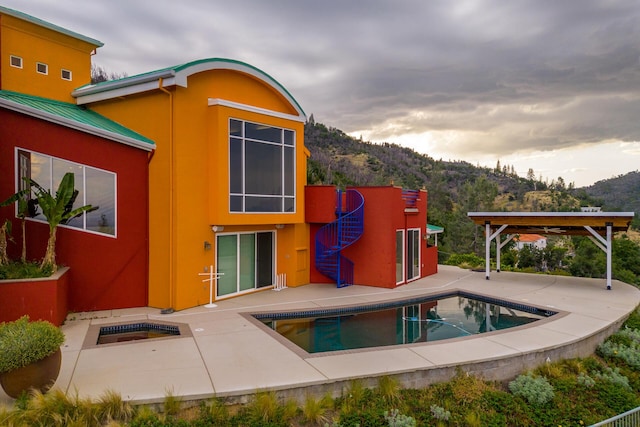 rear view of house with a mountain view, a swimming pool with hot tub, and a patio