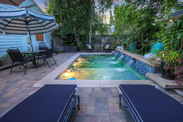 pool at dusk with pool water feature and a patio