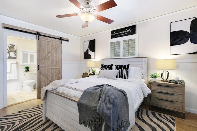 bedroom featuring ensuite bathroom, ceiling fan, a barn door, ornamental molding, and light hardwood / wood-style floors