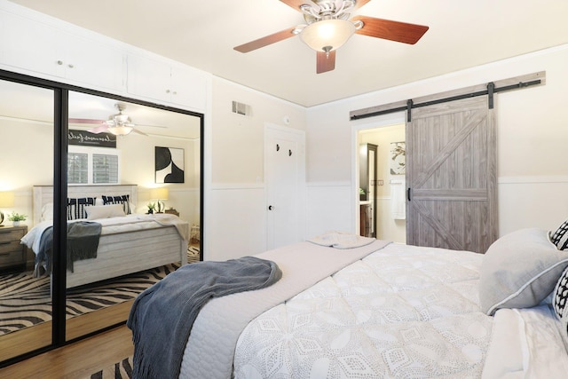 bedroom with hardwood / wood-style floors, ceiling fan, and a barn door