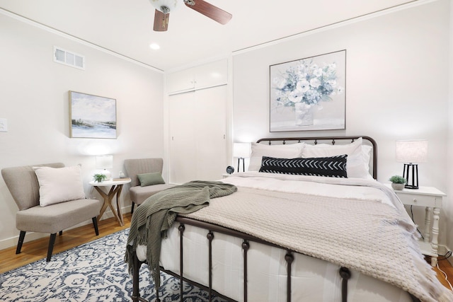 bedroom with ceiling fan, wood-type flooring, ornamental molding, and a closet