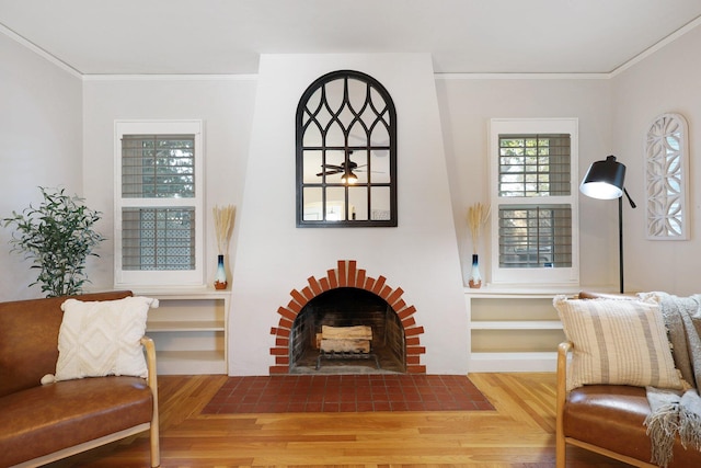 sitting room featuring hardwood / wood-style floors, built in shelves, ornamental molding, and a brick fireplace