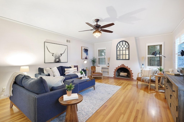 living room with ceiling fan, light hardwood / wood-style floors, ornamental molding, and a brick fireplace