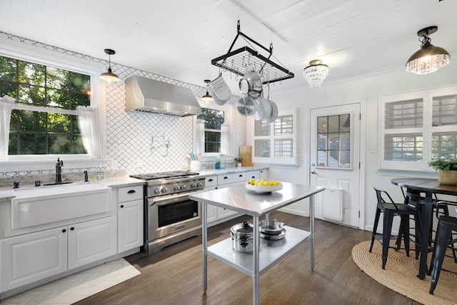 kitchen featuring high end range, tasteful backsplash, wall chimney range hood, pendant lighting, and white cabinetry