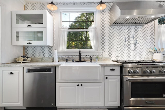 kitchen with appliances with stainless steel finishes, white cabinetry, hanging light fixtures, and wall chimney range hood