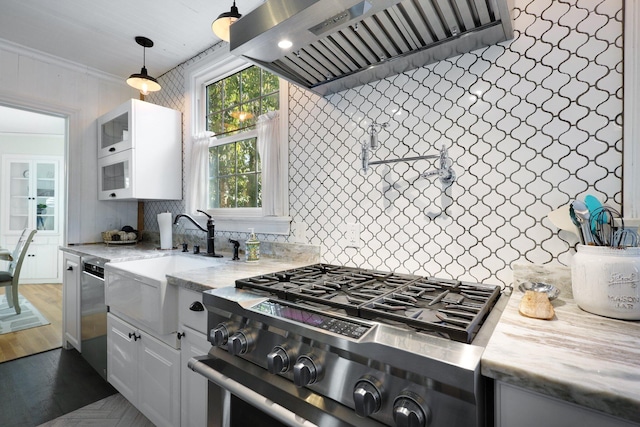 kitchen with appliances with stainless steel finishes, ornamental molding, wall chimney range hood, white cabinetry, and hanging light fixtures