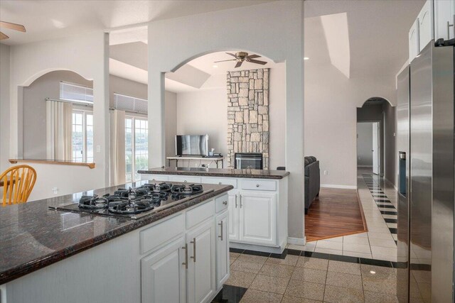 kitchen featuring dark stone counters, a stone fireplace, ceiling fan, white cabinetry, and stainless steel appliances